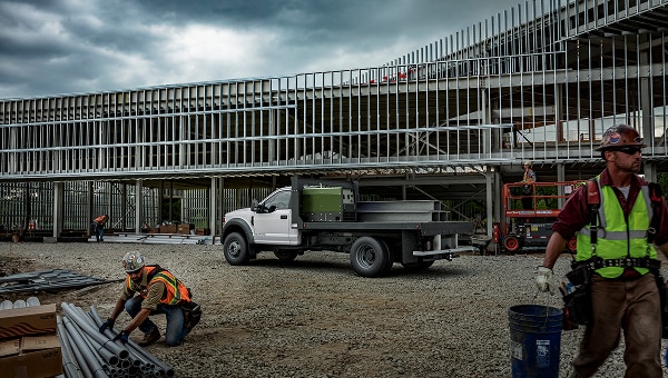 Ford Super Duty Chasis blanca con plataforma de trabajo en un sitio de construcción con estructura metálica y trabajadores.
